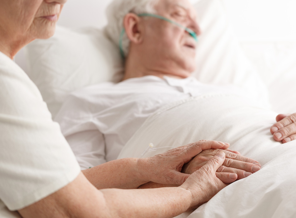 Elderly woman holding mans hand in hospital bed